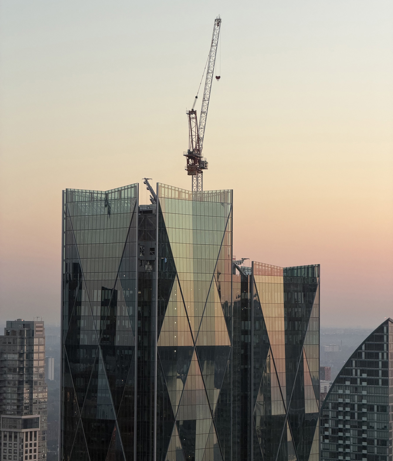 A skyscraper in Toronto with angular glass facade and a crane on top, set against a pastel sunset sky.