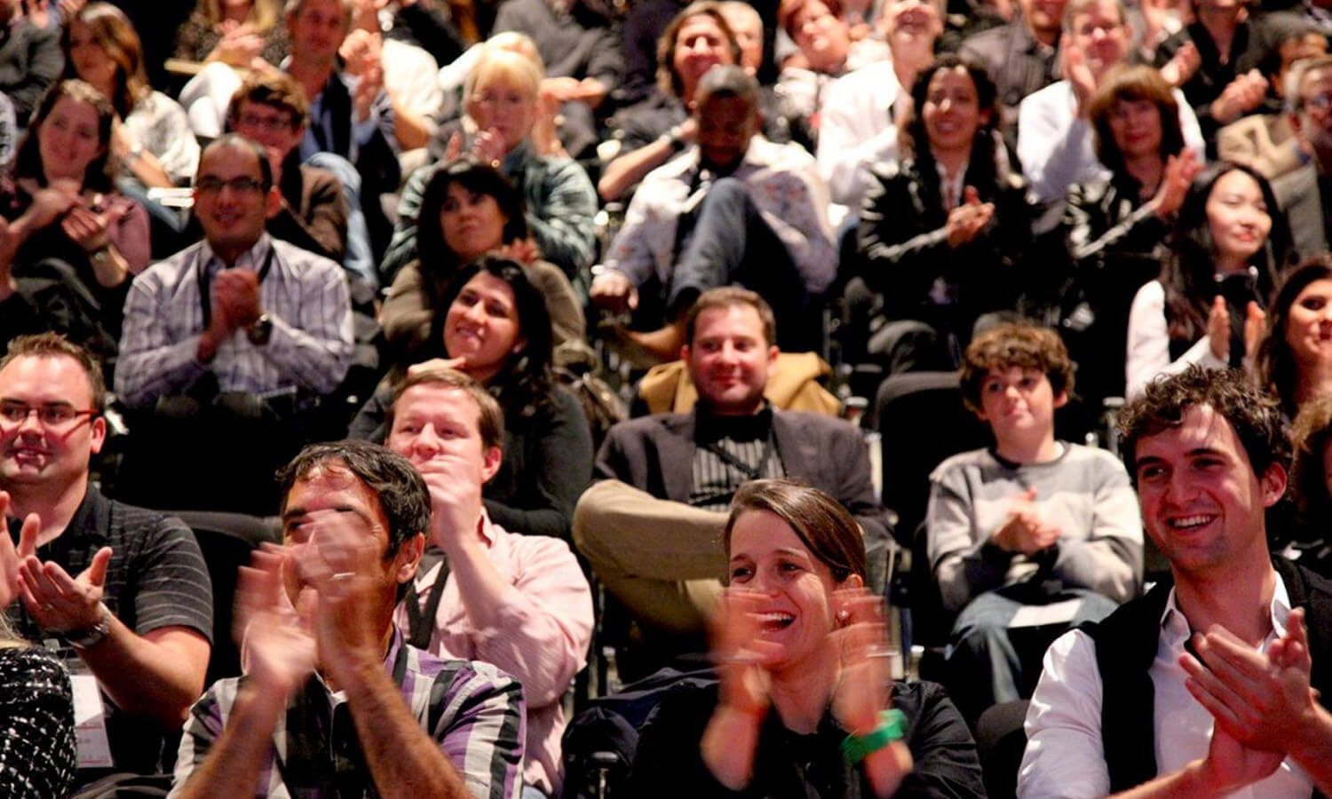 A diverse audience of men and women sit in theater seats, smiling and applauding at the Cusp Conference.