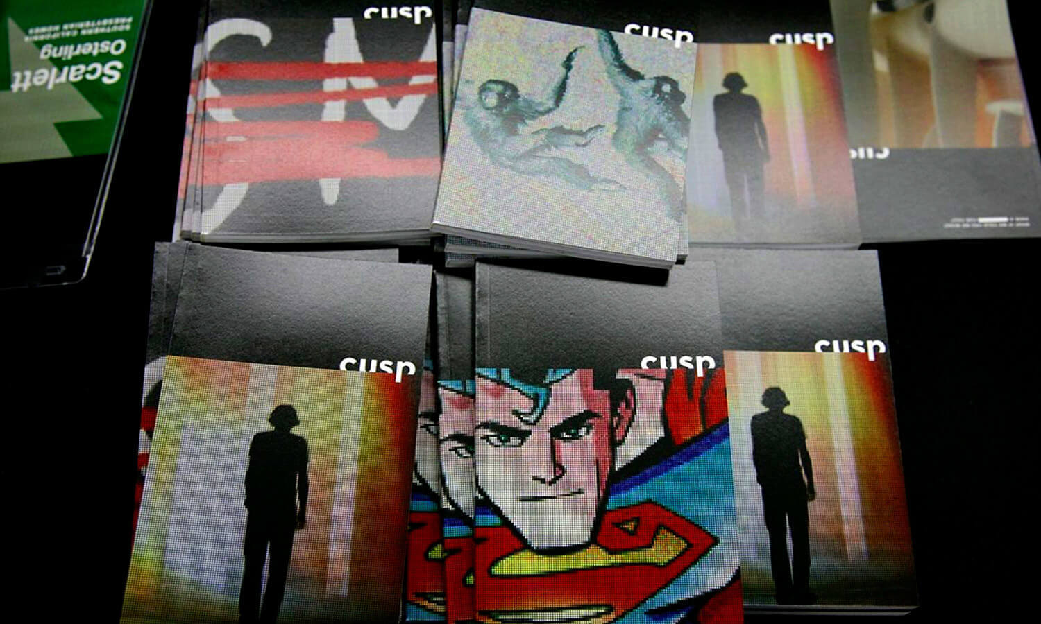 A collection of "Cusp" magazines with vivid covers, featuring art such as a silhouette, abstract shapes, and a superhero.