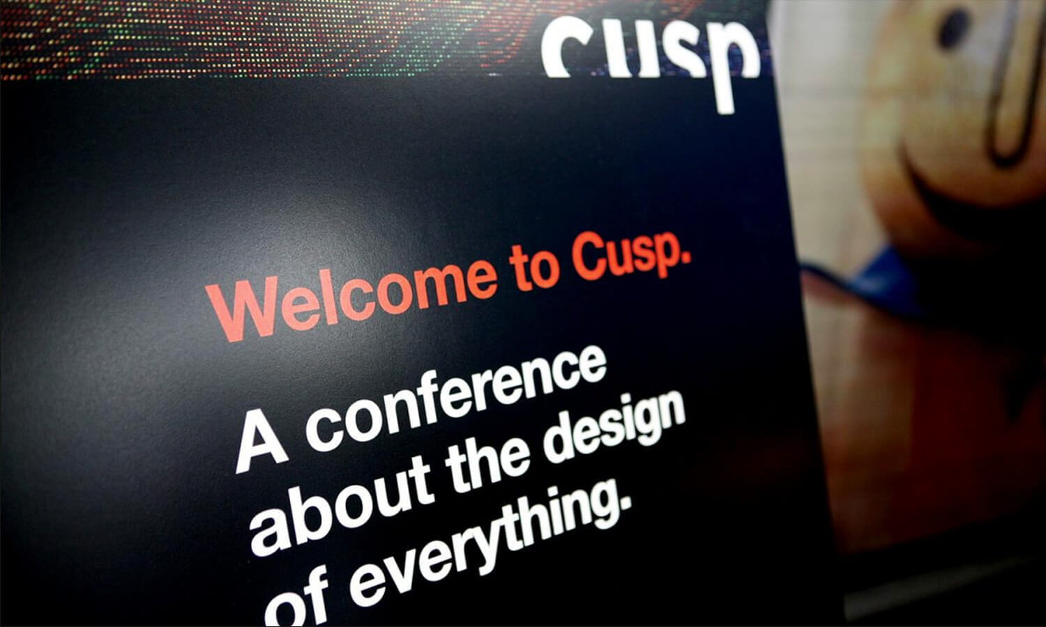 Close-up of a black poster with "Welcome to Cusp." written in orange and white text promoting a design conference.