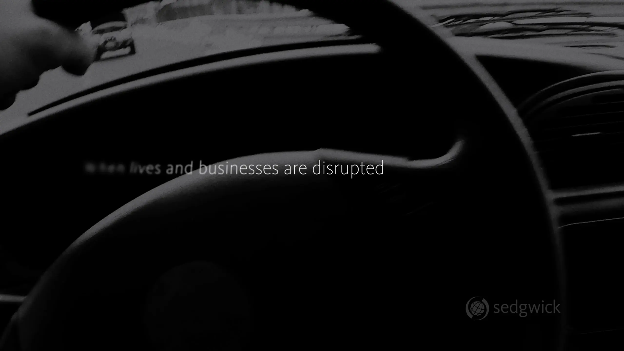Blurred black and white image of a steering wheel, with the text "When lives and businesses are disrupted." A logo says "Sedgwick" at the bottom right.