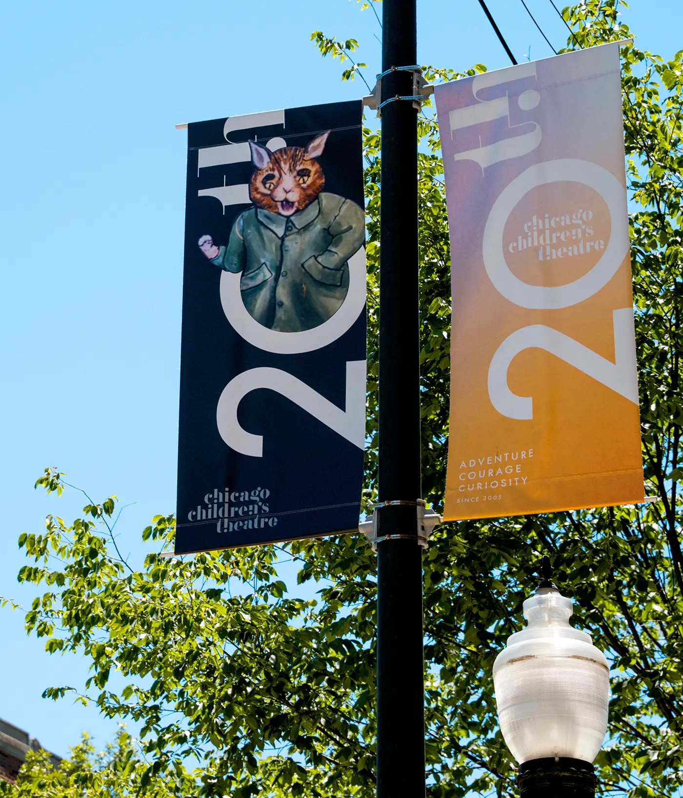 Two vertical banners on a lamppost celebrate the Chicago Children's Theatre's 20th anniversary. One shows a fox in a coat, and the other features text on a bright yellow background.